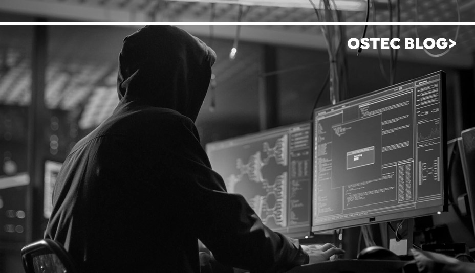 Hacker encapuzado sentado em uma sala escura na frente de dois computadores