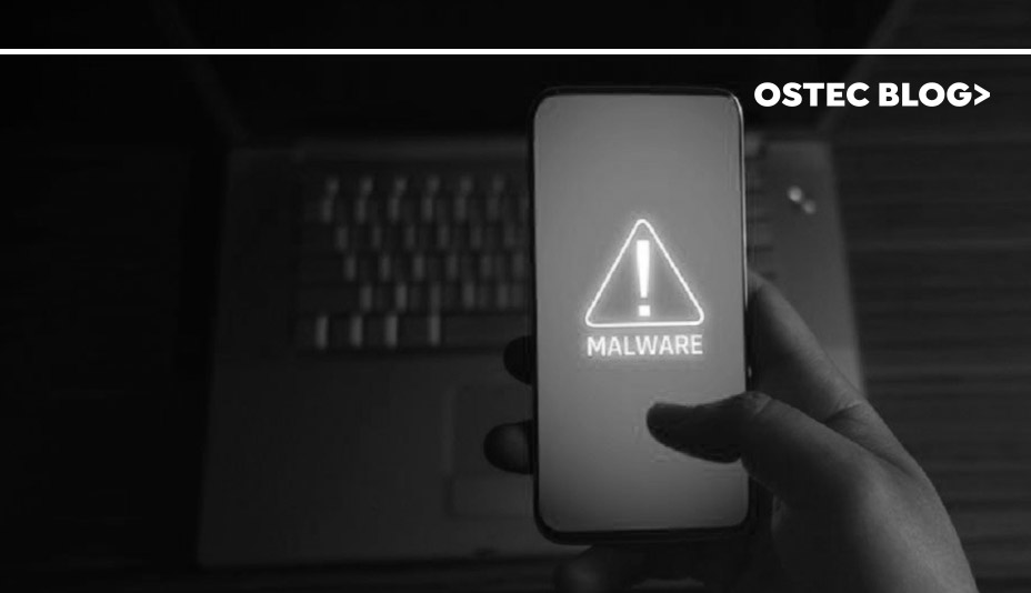 Mão segurando smartphone que apresente uma tela vermelha onde se pode ler em branco a palavra 'malware'.