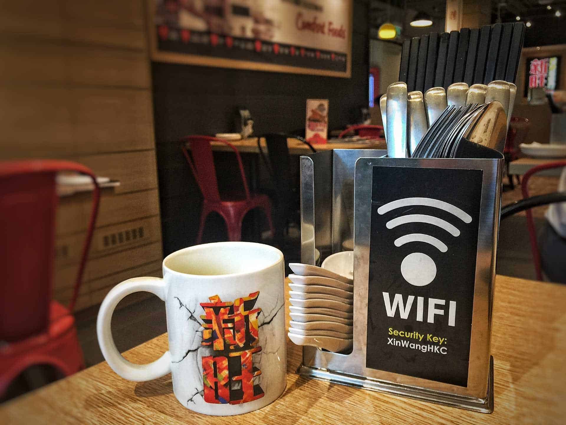 Placa sinalizando que tem Wi-Fi no estabelecimento ao lado de uma xícara sobre uma mesa.